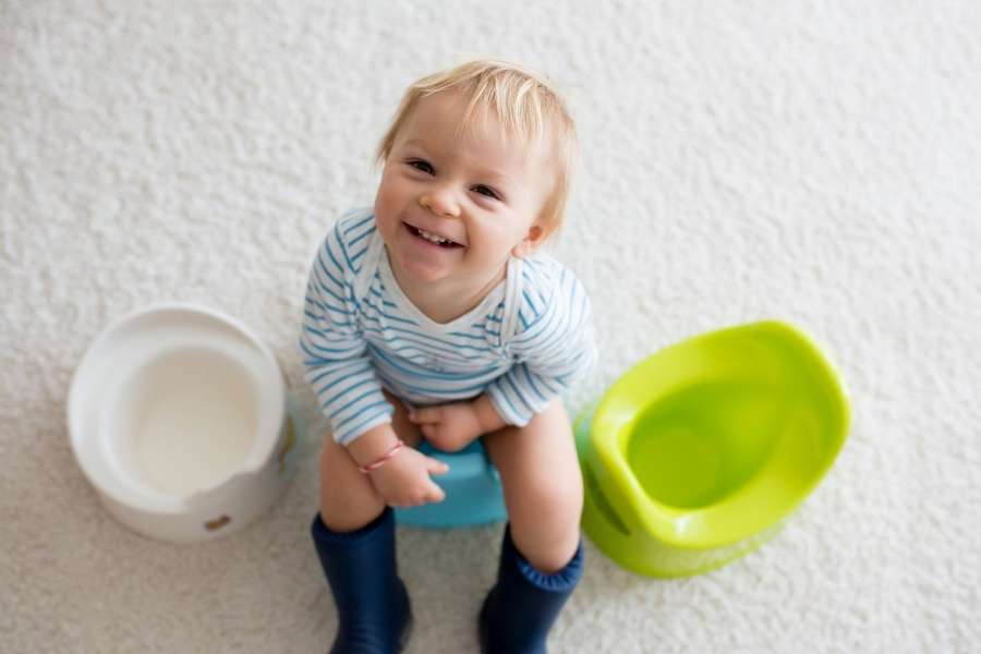 Un petit garçon souriant est assis sur son pot durant son apprentissage de la propreté à la maison.