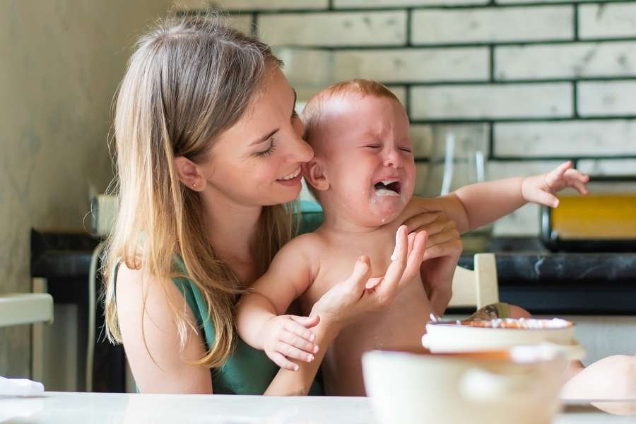 Une mère essayant de consoler son enfant qui pleure pendant le repas, illustrant quand un tout-petit refuse de manger.