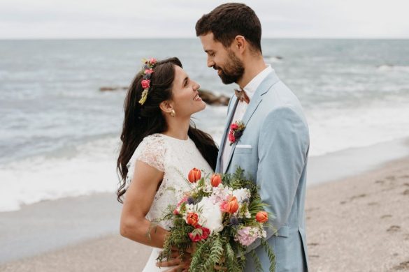 Jeunes mariés souriants en bord de mer après avoir choisi d'organiser une cérémonie de mariage sur la plage.